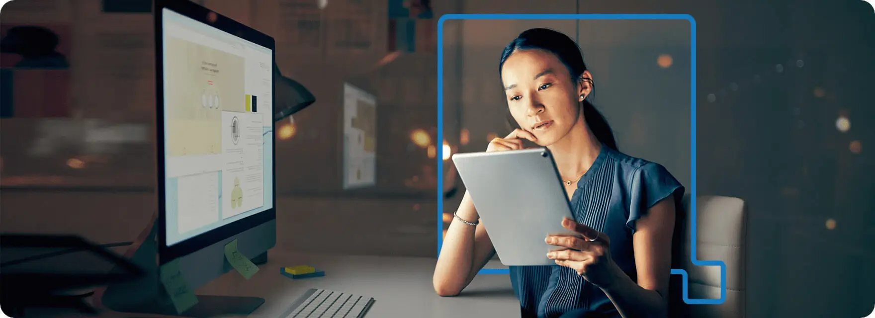 Concept of Female Asian business person reading a document in front of a computer monitor.